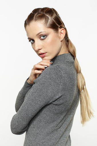 Portrait of beautiful young dark blonde woman. Female with creative braid hairdo on gray background. Girl with hand on shoulder.