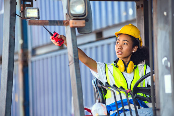 istock Female foreman use radio communication to communicate while driving forklift at shipping container yard. shipping in docks. 1371205981