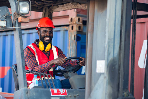 istock Happy male worker in uniform and helmet driving and operating on diesel container forklift truck at commercial dock site. 1371205997