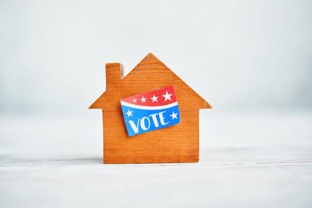 istock Small wooden house with a VOTE sticker in a bright white setting 1371207874