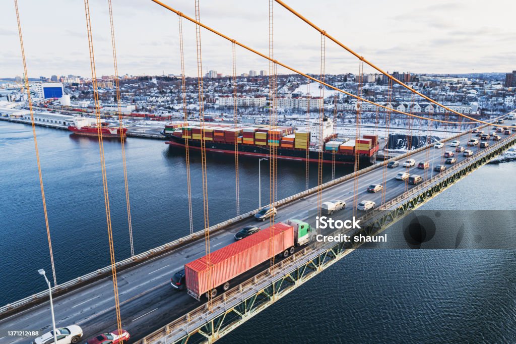 Container Ship Below Rush hour traffic on a bridge above a container ship docked at at pier. Freight Transportation Stock Photo