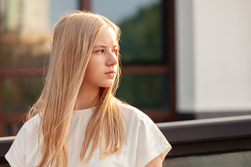 Outdoors portrait of 15 year old blonde teen girl with long hair in white t-shirt