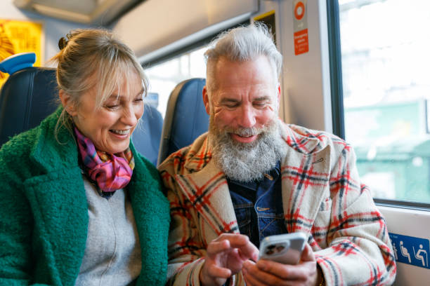 pareja de ancianos activos que usan un teléfono inteligente mientras viajan en tren - senior adult fun autumn senior couple fotografías e imágenes de stock