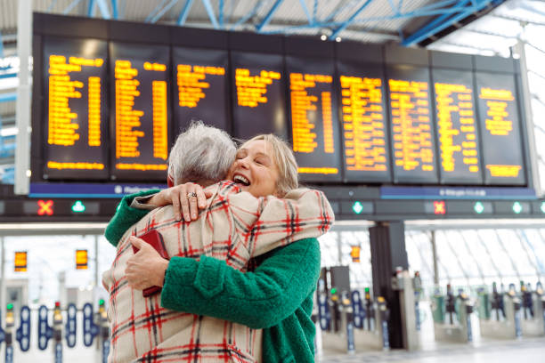 Happy senior couple meeting at airport A vibrant senior woman smiles when greeting and embracing her husband in the terminal of an airport or train station. airport hug stock pictures, royalty-free photos & images