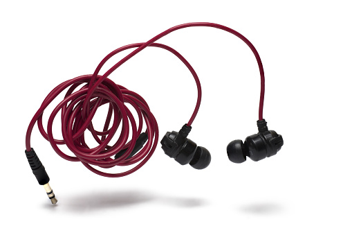 Close up of in ear headphones on red coiled cable with jack plug as connector on white background as concept for listening and enjoying music