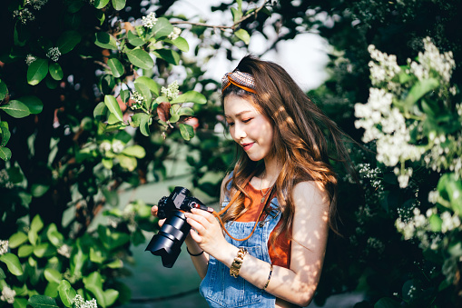 Beautiful Asian female university student photographing nature with camera in park on a sunny day