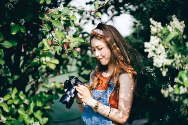 Photo of Beautiful Asian female university student photographing nature with camera in park on a sunny day