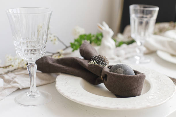 istock Easter egg in bunny napkin on plate with cutlery, bunny, spring flowers on rustic white table. Stylish elegant Easter brunch table setting. Modern table arrangement and eco decoration 1371225551