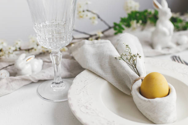 istock Easter egg in bunny napkin on plate with cutlery, bunny, spring flowers on rustic white table. Stylish elegant Easter brunch table setting. Modern table arrangement and eco decoration 1371226208