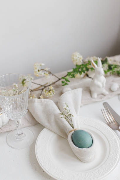 istock Easter egg in bunny napkin on plate with cutlery, bunny, spring flowers on rustic white table. Stylish elegant Easter brunch table setting. Modern table arrangement and eco decoration 1371226542