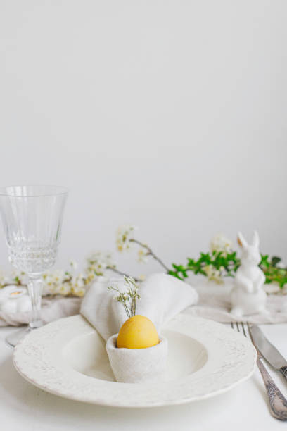 istock Easter egg in bunny napkin on plate with cutlery, bunny, spring flowers on rustic white table. Stylish elegant Easter brunch table setting. Modern table arrangement and eco decoration 1371226688
