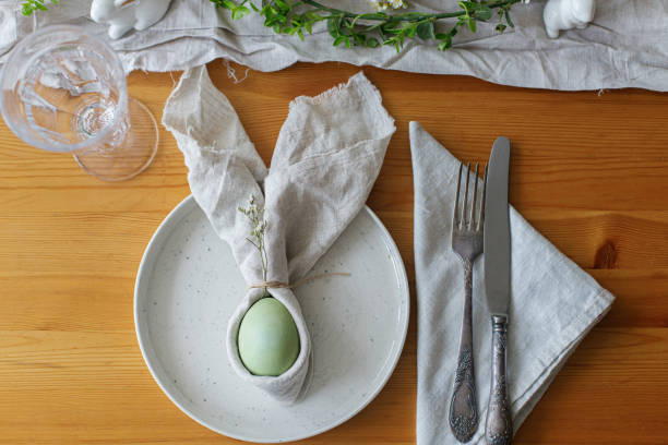 istock Happy Easter! Easter egg in bunny napkin on plate with cutlery, bunny, spring flowers and rustic cloth on wooden table. Top view. Stylish Easter brunch table setting. 1371227258