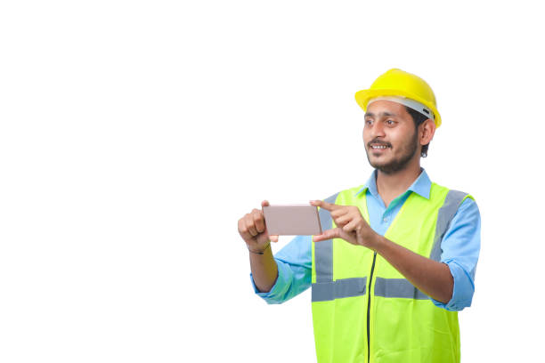 istock Young indian engineer wearing hardhat and using smartphone on white background. 1371232689