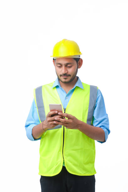 istock Young indian engineer wearing hardhat and using smartphone on white background. 1371232693