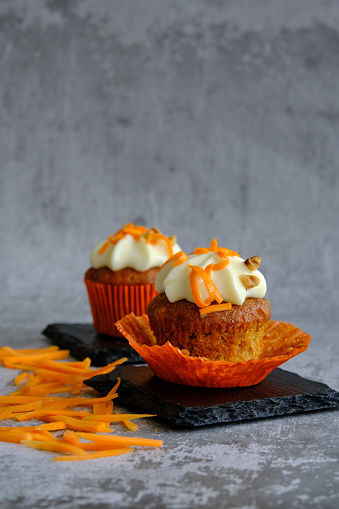 cakes decorated with cream next to grated carrots on a gray background