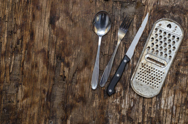 velho ralador de cozinha enferrujado, faca, colher, garfo contra a tábua apodrecendo. utensílios de cozinha de metal. - eating utensil silverware four objects small group of objects - fotografias e filmes do acervo