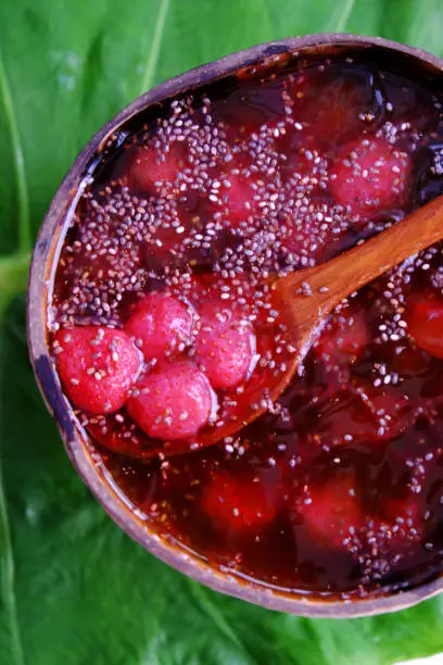 Top view red sugared strawberries in bowl that make from coconut shell on green leaf, red fresh Da Lat fruit for summer day, yummy food