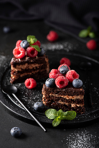slices of homemade chocolate cake with fresh fruit on a black plate, top view