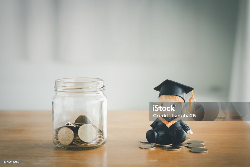 education savings concept Education savings concept. Coins in a glass jar for education money savings with a graduate doll. Personal financial planning for the future. Tuition Stock Photo