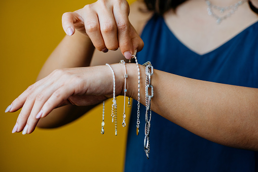 Close-up shot of women's choose silver bracelets on her hands on a yellow background. Entrepreneur's hand arranging the jewels to get the product ready and send it to her client .