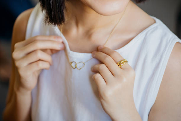 portrait of a gorgeous young asian woman trying on a gold necklace - hand gold jewels bildbanksfoton och bilder