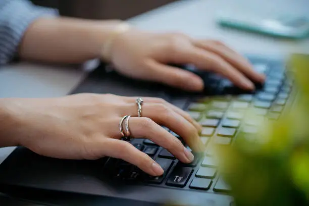 Fashionable woman with luxury accessories such as diamond ring and silver bracelet while working on laptop at desk.