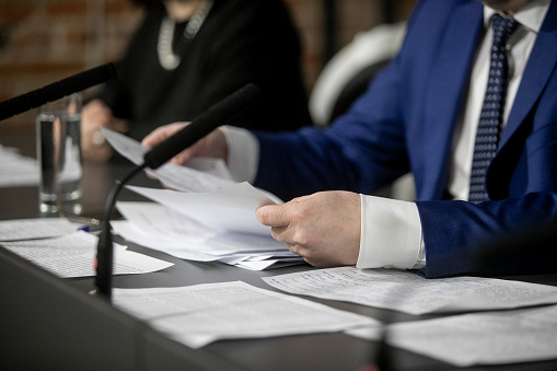 A man in a business suit is holding a pen. There are notebooks on the table