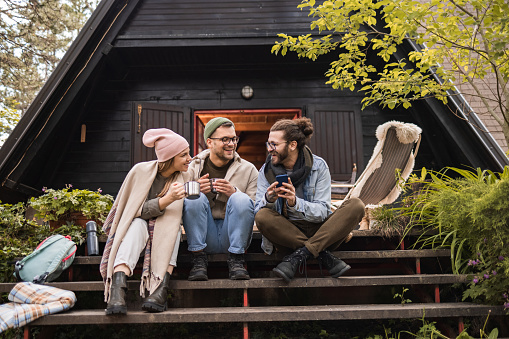 Group of happy friends talking while reading a text message on a patio in front of a log cabin.