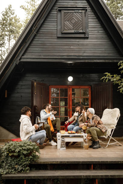 Young happy friends talking on a patio in front of cottage. Group of happy friends enjoying in conversation at cabin's patio. cottage life stock pictures, royalty-free photos & images