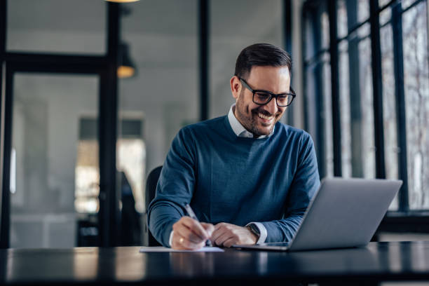 Happy caucasian man in a blue sweater, checking the budget of his company. Excited adult man, happy with the income his business made. blue business stock pictures, royalty-free photos & images
