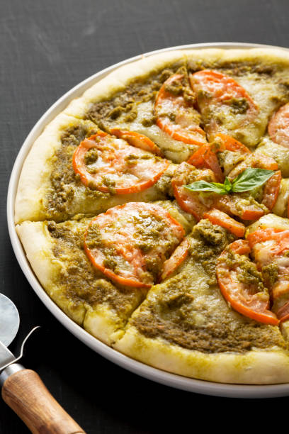 istock Homemade Pesto Pizza with Fresh Tomatoes and Mozzarella on a black background, low angle view. 1371258314