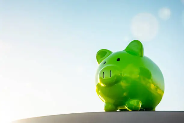 Green piggy bank against blue sky background concept for saving, accounting, banking and business account or sustainable and environmentally friendly finance
