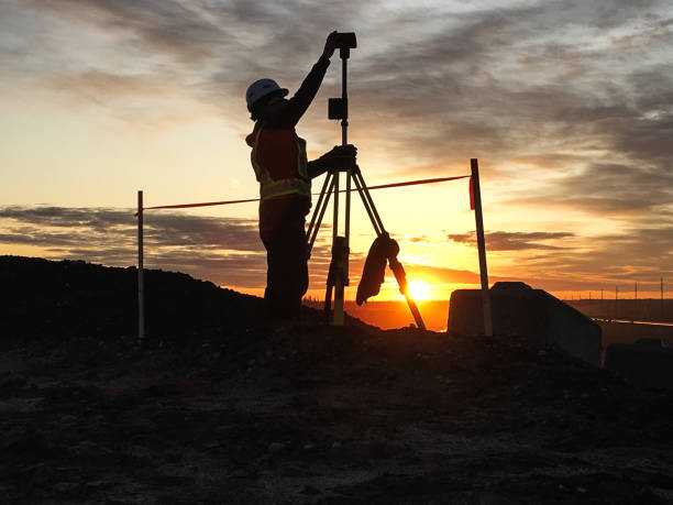 Silhouette land surveyor setting up total station at a mine site in Fort McMurray, Alberta