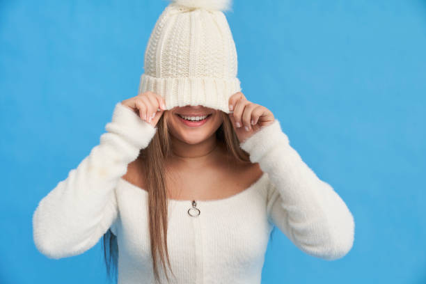 Happy young female in warm clothes smiling and looking at camera while standing on blue background in studio