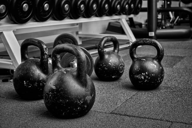 Dumbbells and kettlebells on a floor. Bodybuilding equipment. Fitness or bodybuilding concept background. black and white photography Dumbbells and kettlebells on a floor. Bodybuilding equipment. Fitness or bodybuilding concept background. black and white photography kettlebell stock pictures, royalty-free photos & images