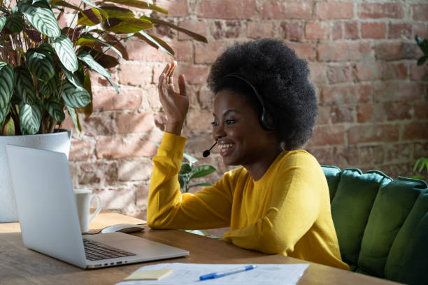 employée afro souriante parlant dans le chat vidéo avec des clients sur ordinateur portable, regardant le webinaire à la maison - working smiling equipment car photos et images de collection