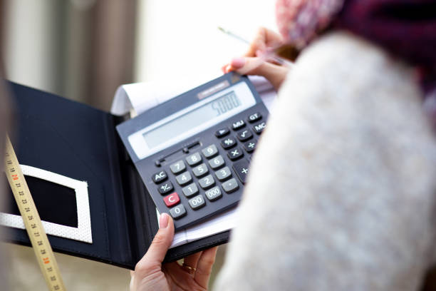 Unrecognizable woman in upper garments making calculations using calculator, measuring tape writing notes on notebook. Construction, real estate, building, counting, budgeting, repairing concept.