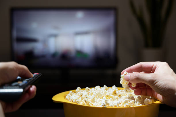 istock Man's hand grabbing popcorn from a yellow bowl while changing TV channels 1371280991