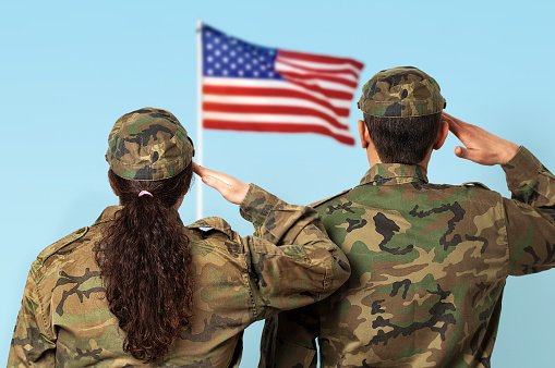 Rear view shot of two US soldiers saluting the US flag.