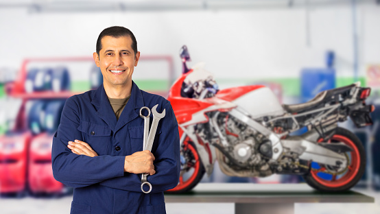 Front view portrait of a motorcycle mechanic posing standing looking at you in a mechanical workshop and copy space