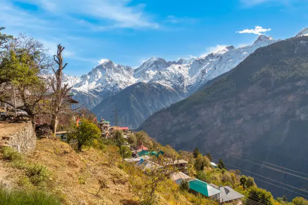 Aerial view of scenic mountain village with residential houses with majestic Kinnaur Kailash Himalaya range on way to Chitkul, Himachal Pradesh, India