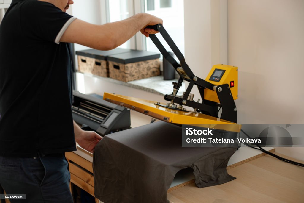 Cropped man worker back using heat thermal textile application transfer press. Printing application black T-shirt. Side Cropped man worker side back using heat thermal textile application transfer press. Printing application black T-shirt design. Printing house office offset equipment. Manufacturing business fabric Printing Press Stock Photo Cropped man worker back using heat thermal textile application transfer press. Printing application black T-shirt. Side Cropped man worker side back using heat thermal textile application transfer press. Printing application black T-shirt design. Printing house office offset equipment. Manufacturing business fabric Printing Press Stock Photo