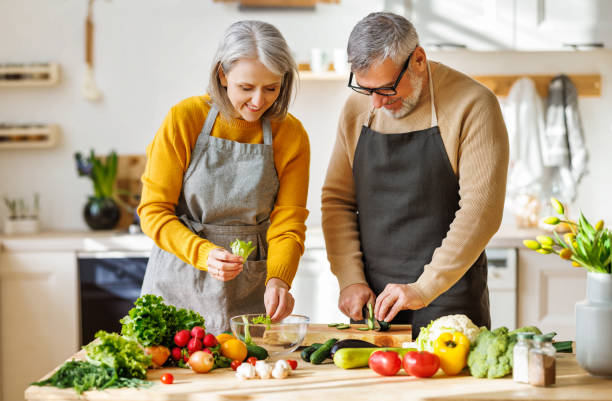 un couple de personnes âgées heureux prépare un dîner végétarien ensemble, en coupant des légumes frais colorés - cooking senior adult healthy lifestyle couple photos et images de collection