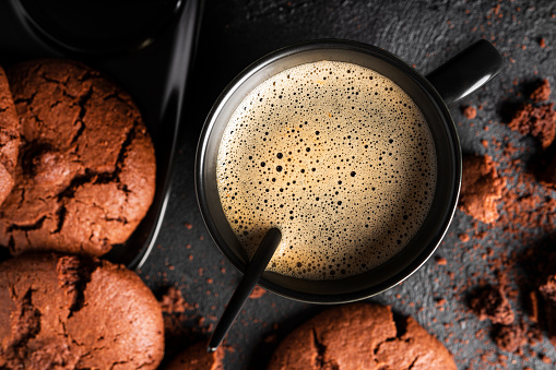 Coffee americano in cup on dark background. Hot coffee with foam. Coffee with chocolate cookie. High quality photo