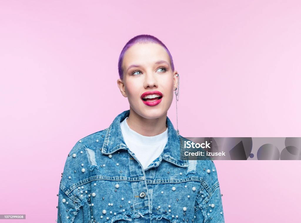 Young woman with short purple hair Headshot of surprised young woman wearing denim jacket, looking away and smiling. Studio shot on pink background. Generation Z Stock Photo
