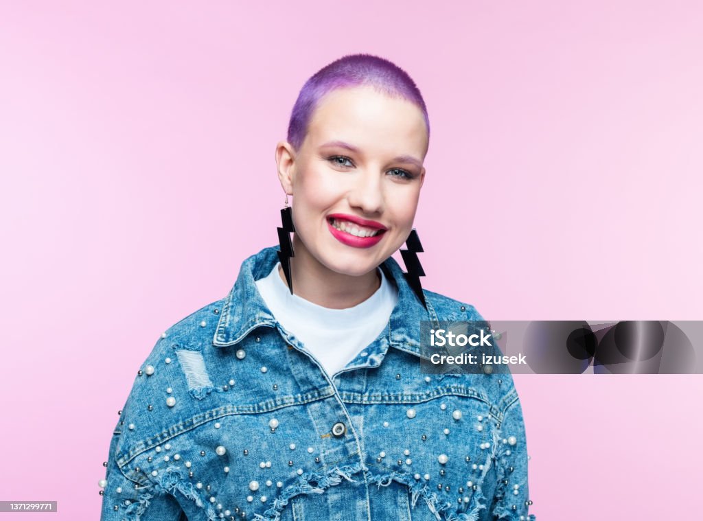 Young woman with short purple hair Headshot of cheerful young woman wearing denim jacket, smiling at camera. Studio shot on pink background. Purple Hair Stock Photo