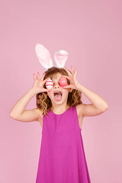 istock Delighted child covering eye with eggs during Easter party in pink studio 1371302074