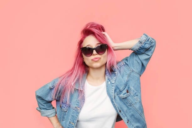 A young stylish woman with pink hair in a denim jeans jacket, sunglasses poses with her hand on head A young stylish woman with pink hair in a white t-shirt, blue denim jeans jacket, black sunglasses poses with her hand on a head isolated on a color light pink background. Beauty, fashion pink hair stock pictures, royalty-free photos & images