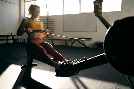 In the modern gym, strong and dedicated Caucasian sportswoman, exercising on the rowing machine