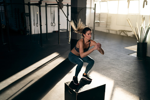 At the gym, modern and active young woman jumping on the big box